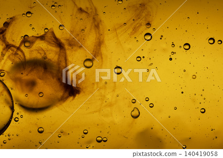 Macro shot of textured amber liquid with floating oil droplets and swirling dark ink patterns Macro shot of textured amber liquid with floating oil droplets and swirling dark ink patterns 140419058