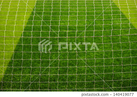 Close-up detail of a white soccer goal net grid against a blurred green grass field background Close-up detail of a white soccer goal net grid against a blurred green grass field background 140419077
