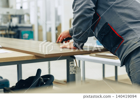 Craftsman measures wood in furniture workshop for building project during daytime work hours Craftsman measures wood in furniture workshop for building project during daytime work hours 140419094