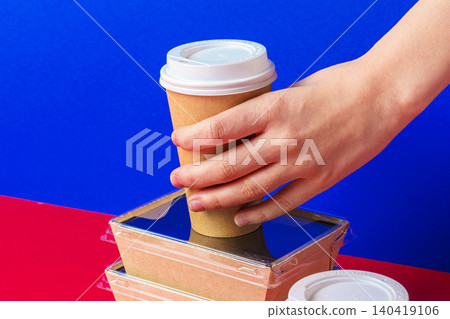 Hand reaches for coffee cup placed on food containers with blue and red background Hand reaches for coffee cup placed on food containers with blue and red background 140419106