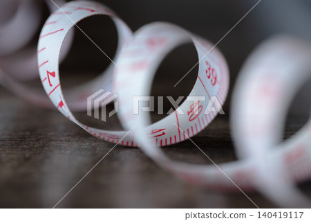 Soft focus macro of a white tailor's tape measure spiraling on a rustic wooden surface Soft focus macro of a white tailor's tape measure spiraling on a rustic wooden surface 140419117