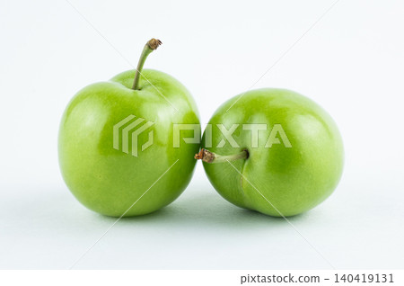 Pair of ripe green greengage plums with stems on a bright white background, studio composition Pair of ripe green greengage plums with stems on a bright white background, studio composition 140419131