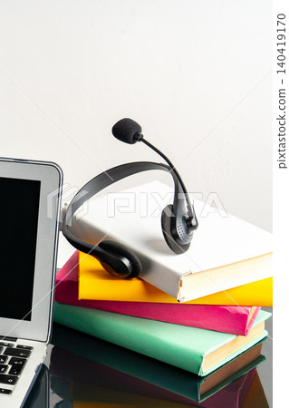 Headset rests on a stack of books near a laptop during study time 140419170