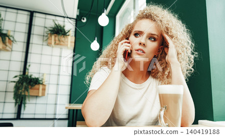Woman receiving a scam call while sitting in a cafe during the day Woman receiving a scam call while sitting in a cafe during the day 140419188