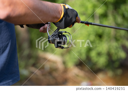 A person with a fishing rod stands by water and greenery 140419231