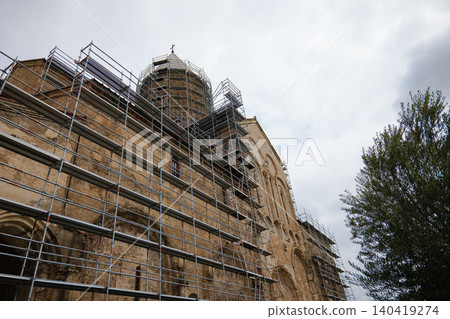 Wide shot of a medieval cathedral under renovation against a cloudy sky. Neutral lighting Wide shot of a medieval cathedral under renovation against a cloudy sky. Neutral lighting 140419274