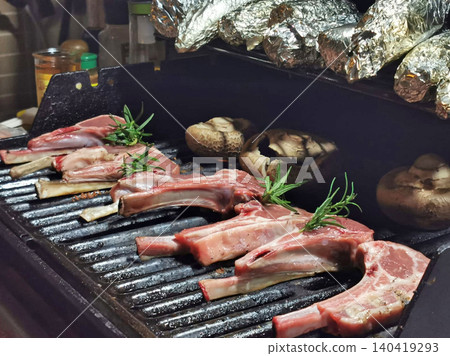 Delicious lamb chops and mushrooms cooking on a hot grill with rosemary sprigs Delicious lamb chops and mushrooms cooking on a hot grill with rosemary sprigs 140419293