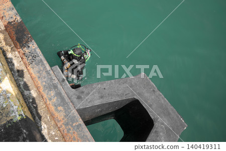 High angle shot of a professional scuba diver in black wetsuit inspecting a concrete harbor dock High angle shot of a professional scuba diver in black wetsuit inspecting a concrete harbor dock 140419311