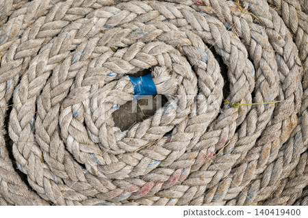 Top view of a thick, weathered nautical rope coiled in a spiral pattern with blue tape Top view of a thick, weathered nautical rope coiled in a spiral pattern with blue tape 140419400