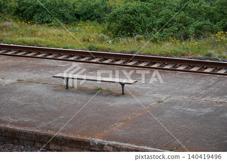 A minimalist view of a weathered stone bench at a train station with tracks and greenery A minimalist view of a weathered stone bench at a train station with tracks and greenery 140419496