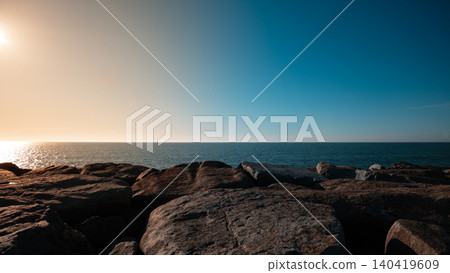 Wide-angle shot of a stone breakwater under a vibrant gradient sky at golden hour 140419609