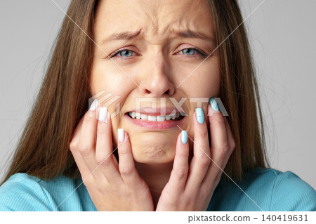 Woman expresses sadness while holding her face with hands in a studio setting Woman expresses sadness while holding her face with hands in a studio setting 140419631