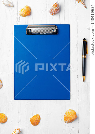 Blue clipboard on a table with seashells and a pen around it 140419684