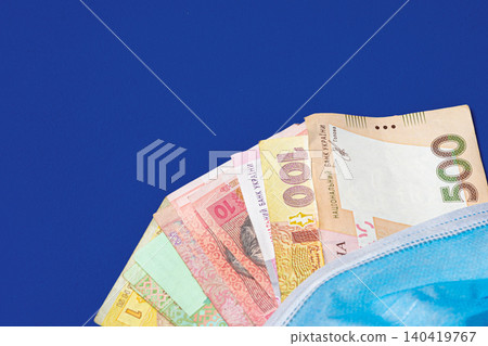 Currency from Ukraine placed under a medical mask on a blue surface 140419767