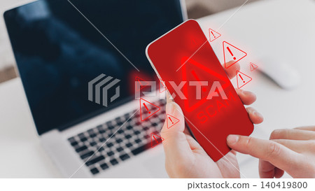 Message shows scam warning on phone screen near laptop during daytime Message shows scam warning on phone screen near laptop during daytime 140419800