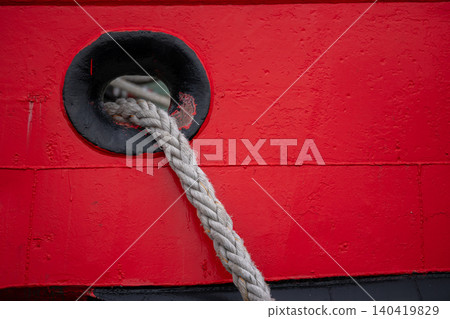 Detail of a grey synthetic rope passing through a black hawsehole on a vibrant red vessel Detail of a grey synthetic rope passing through a black hawsehole on a vibrant red vessel 140419829