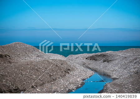 Natural stream cutting through grey pebbles leading to the blue ocean under a clear sky Natural stream cutting through grey pebbles leading to the blue ocean under a clear sky 140419839