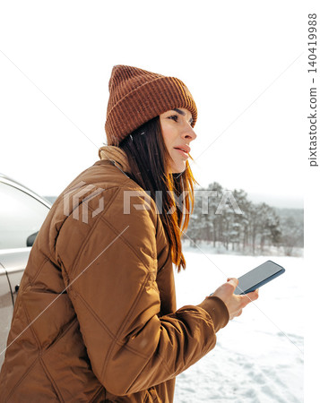Woman stands outside in snow while using her smartphone in winter setting Woman stands outside in snow while using her smartphone in winter setting 140419988