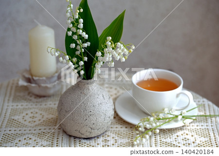 Delicate white lily of the valley flowers with a white ceramic cup of tea Delicate white lily of the valley flowers with a white ceramic cup of tea 140420184