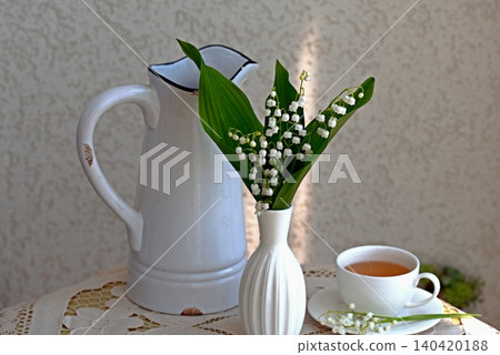 Delicate white lily of the valley flowers with a white ceramic cup of tea Delicate white lily of the valley flowers with a white ceramic cup of tea 140420188