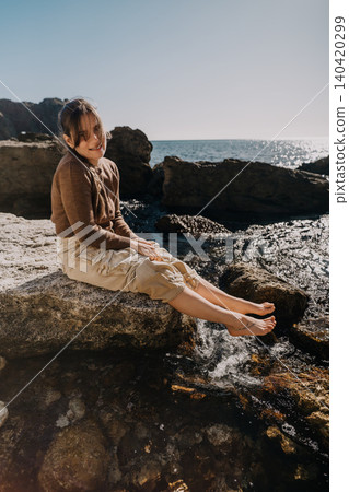 Woman coast rocks young woman sitting on the seashore rocks on a sunny day with her bare feet near the water Woman coast rocks young woman sitting on the seashore rocks on a sunny day with her bare feet near the water 140420299
