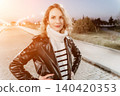 Woman leather jacket portrait standing confidently on a paved park path at dusk under evening street lights 140420353