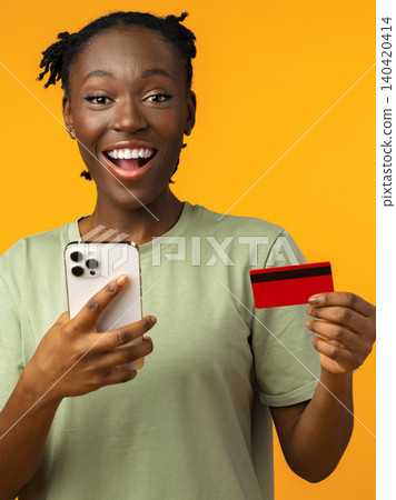 Joyful person holding a phone and a credit card in front of a bright background 140420414