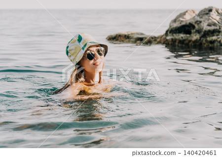 Woman, Sea, Summer: A woman wearing a bucket hat swims in the sea on a sunny day. Woman, Sea, Summer: A woman wearing a bucket hat swims in the sea on a sunny day. 140420461