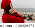 Woman beret sea posing in a red sweater against an ocean background with eyes closed reflecting a peaceful and calm mood 140420473