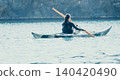 Kayaking Woman Paddle Lake - A woman paddles a kayak on a calm lake with a forested background. 140420490