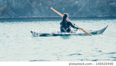 Kayaking Woman Paddle Lake - A woman paddles a kayak on a calm lake with a forested background. Kayaking Woman Paddle Lake - A woman paddles a kayak on a calm lake with a forested background. 140420490