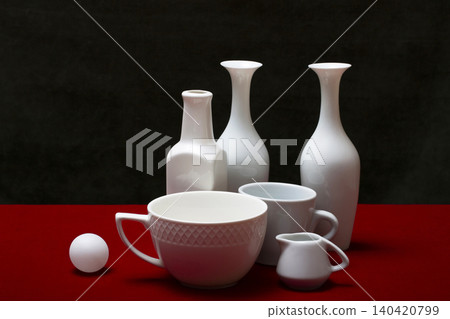 Still life with white dishes on a table with a red cover. Still life with white dishes on a table with a red cover. 140420799