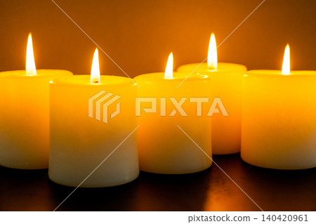 Warm glow from lit candles arranged in a row on a dark surface at night Warm glow from lit candles arranged in a row on a dark surface at night 140420961