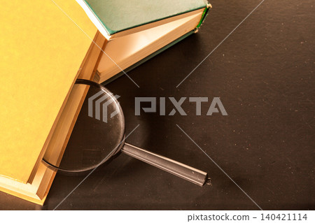 Books and a magnifying glass on a dark table with bright light coming from the side Books and a magnifying glass on a dark table with bright light coming from the side 140421114
