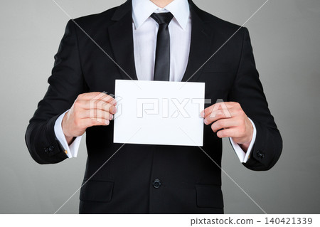 Businessman holds blank paper against gray background in office setting during daytime 140421339