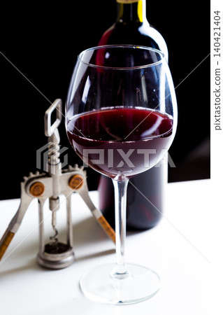 Red wine in a glass next to an open bottle and corkscrew on a table Red wine in a glass next to an open bottle and corkscrew on a table 140421404