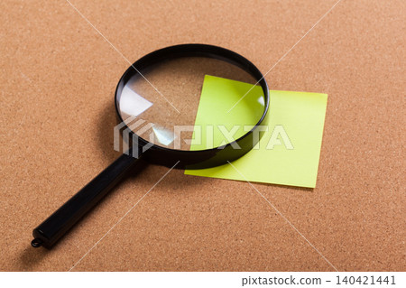 Magnifying glass on a green sticky note placed on a cork board Magnifying glass on a green sticky note placed on a cork board 140421441