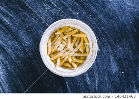Cooked pasta sits in a bowl on a black surface with flour scattered around 140421468
