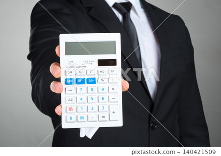 Man in suit holds calculator with one hand in a simple setting Man in suit holds calculator with one hand in a simple setting 140421509