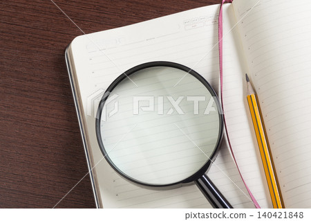 Notebook with a magnifying glass and a pencil placed on a wooden table Notebook with a magnifying glass and a pencil placed on a wooden table 140421848