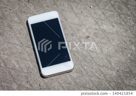 Smartphone lying on the ground with cracked screen near a textured surface in daylight Smartphone lying on the ground with cracked screen near a textured surface in daylight 140421854