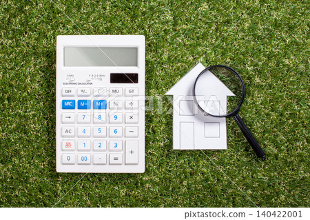 Calculator and magnifying glass next to house drawing on green grass Calculator and magnifying glass next to house drawing on green grass 140422001