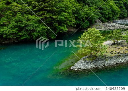 Surrounded by mountains of deep green foliage, a small island and trees float in an emerald green river. Surrounded by mountains of deep green foliage, a small island and trees float in an emerald green river. 140422209