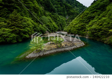 Surrounded by mountains of deep green foliage, a small island and trees float in an emerald green river. Surrounded by mountains of deep green foliage, a small island and trees float in an emerald green river. 140422210