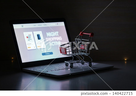 Shopping online at night with a laptop and a small shopping cart 140422715