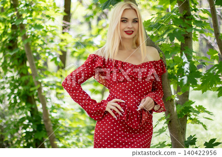 Smiling Blonde Woman in Red Dress by Tree 140422956