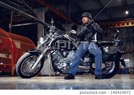 Biker man in leather jacket and helmet sitting on his motorcycle Biker man in leather jacket and helmet sitting on his motorcycle 140424072