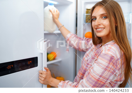 Portrait of a young blonde woman taking food from her fridge 140424233