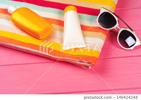 Colorful striped towel with sunscreen cream and sunglasses on pink wooden background Colorful striped towel with sunscreen cream and sunglasses on pink wooden background 140424248