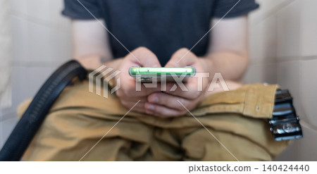 Man sitting on the toilet with a smartphone in hands. Guy scrolling phone on the loo, concept of prolonged sitting risk, screen addiction, and hemorrhoids. Man sitting on the toilet with a smartphone in hands. Guy scrolling phone on the loo, concept of prolonged sitting risk, screen addiction, and hemorrhoids. 140424440